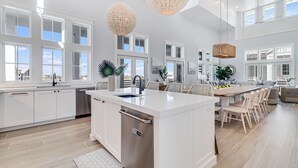 Une cuisine spacieuse dotée d’un îlot central, de grandes fenêtres et de luminaires suspendus modernes.