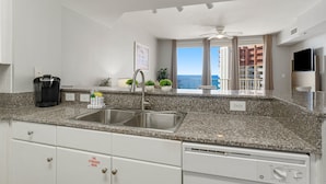 A modern kitchen with granite countertops, stainless steel sink, and white cabinetry. - Shores of Panama by Blue Swell (Panama City Beach)
