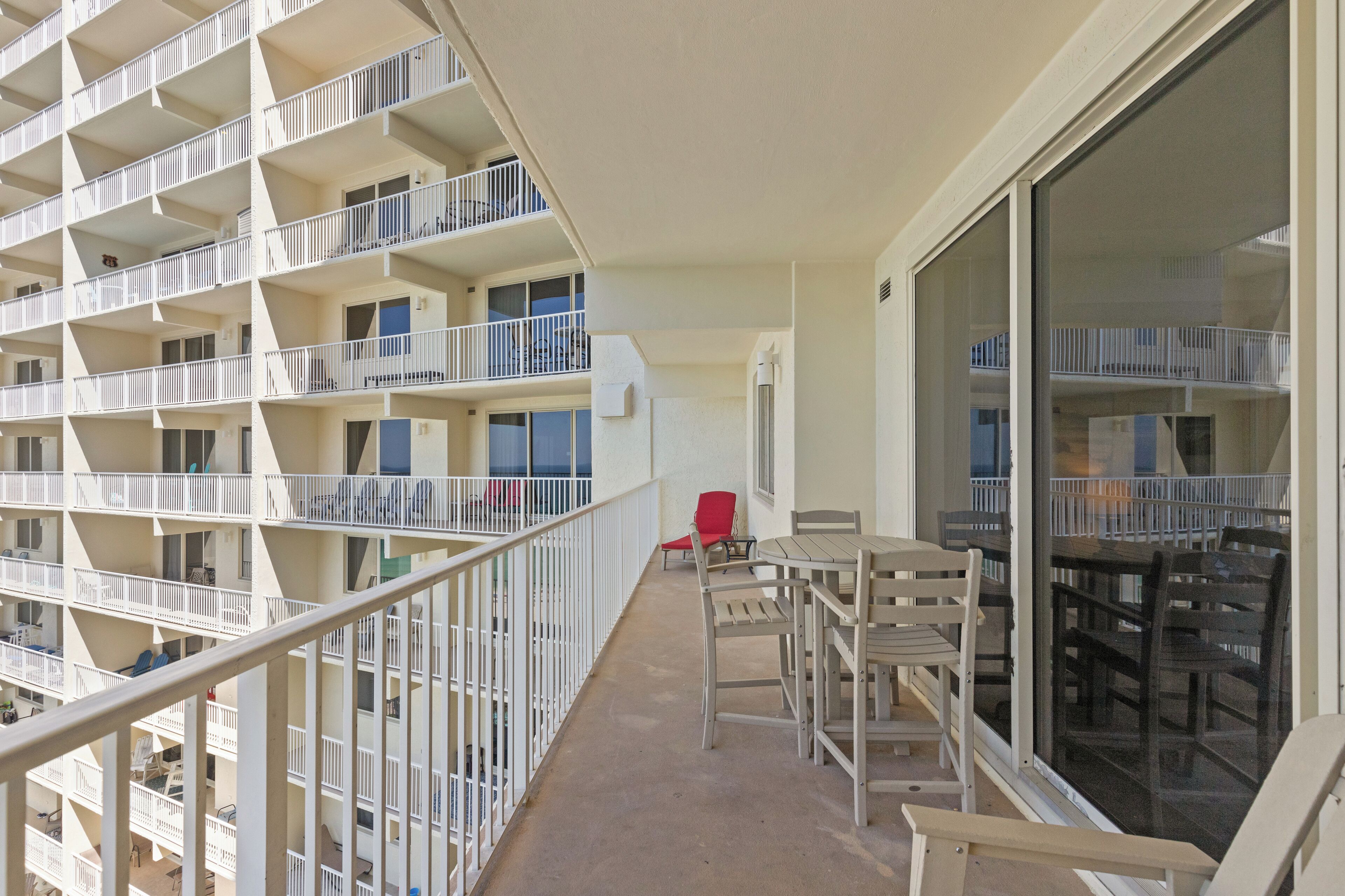 A multi-story hotel balcony with white railings, a dining table with chairs, and a red chair.