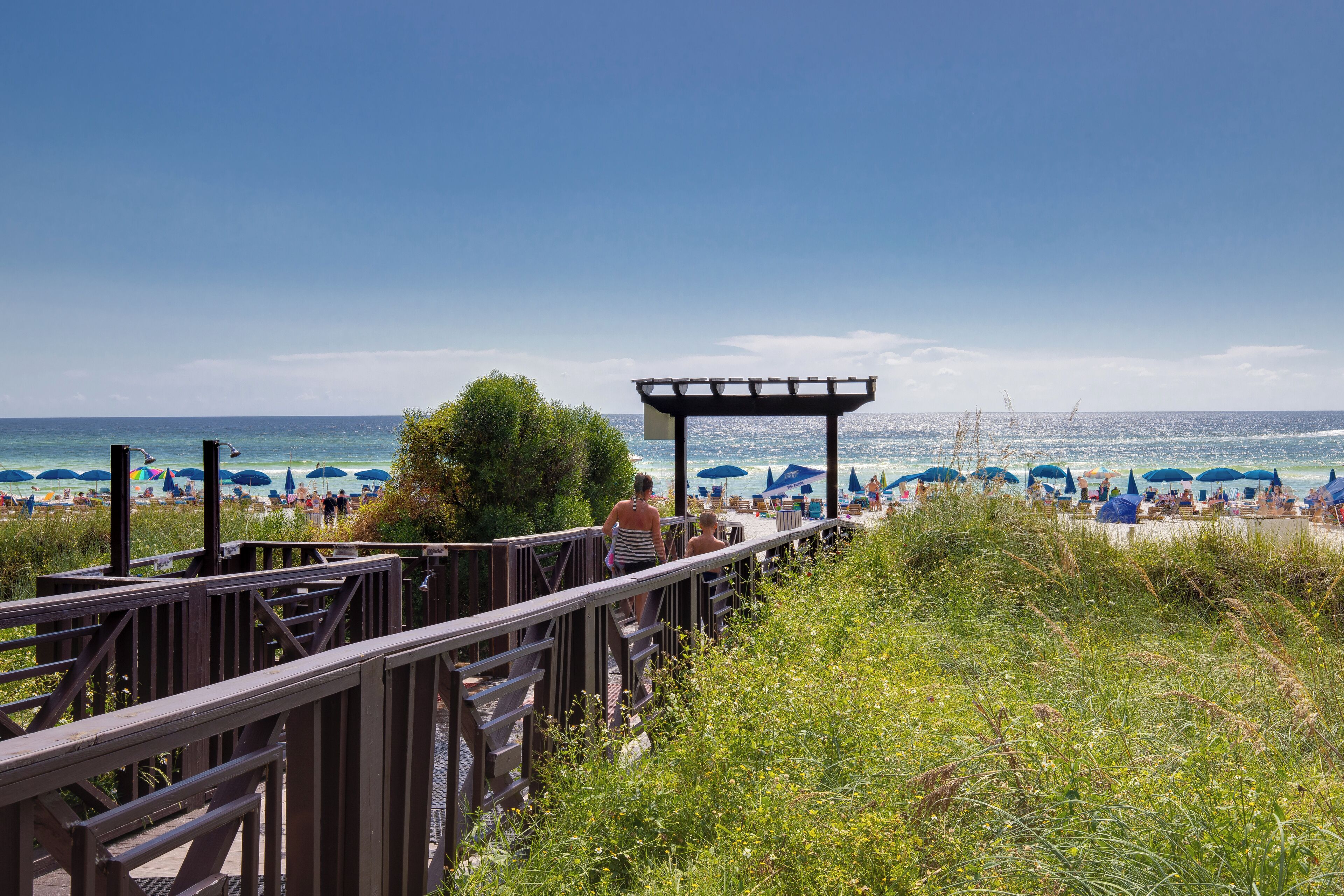 A wooden deck leading to a beach with umbrellas and people.