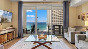 A living room with a glass coffee table, a sofa, a TV, and a view of the beach and ocean through large sliding doors. - Shores of Panama by Blue Swell (Panama City Beach)