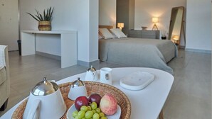 Een moderne hotelkamer met een bed, nachtkastje en een ontbijttafel met fruit en een theepot.