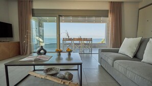 Een moderne woonkamer met een bank, salontafel en uitzicht op de zee door grote glazen deuren.