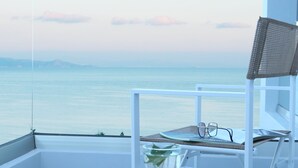 Een balkon met uitzicht op zee, een stoel, een dienblad met een glas water en een paar brillen.