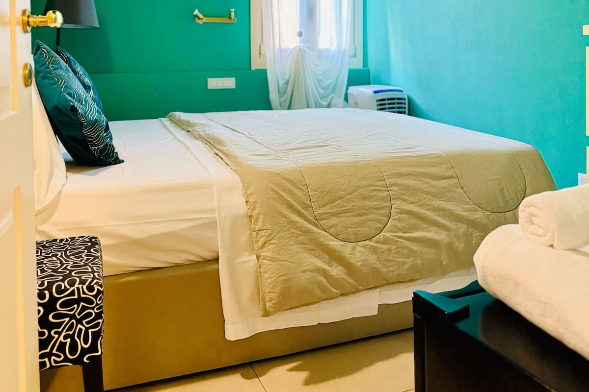 A room with a bed, a bedside table, a lamp, and a window with curtains.