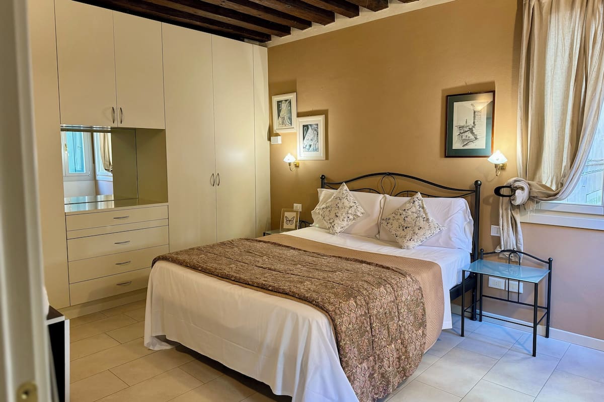 A bedroom with a bed, a wardrobe, a bedside table, and a window with curtains.
