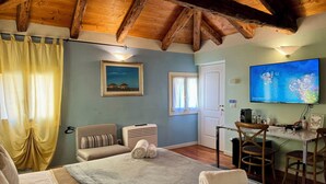 Quarto com cama, escrivaninha, cadeira, televisão e janela com cortinas.