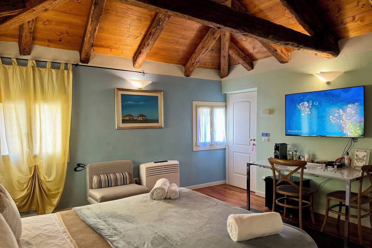 A bedroom with a bed, a desk, a chair, a television, and a window with curtains.