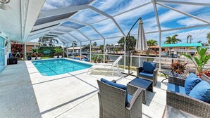 A covered outdoor pool area with lounge chairs and a view of the marina. - Hometown Paradise- Canalfront home with dock and heated pool  (Bradenton)