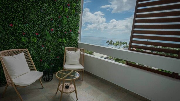 A balcony with two wicker chairs, a small round table, and a green wall with red flowers. - Bel Appartement vue mer - Mafat'appart (La Possession)
