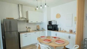 A compact kitchen with white cabinets, a stainless steel refrigerator, a microwave, and a dining area with a round table and white chairs. - Bel Appartement vue mer - Mafat'appart (La Possession)