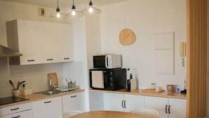 A compact kitchen with white cabinets, a wooden dining table, and white chairs. - Bel Appartement vue mer - Mafat'appart (La Possession)