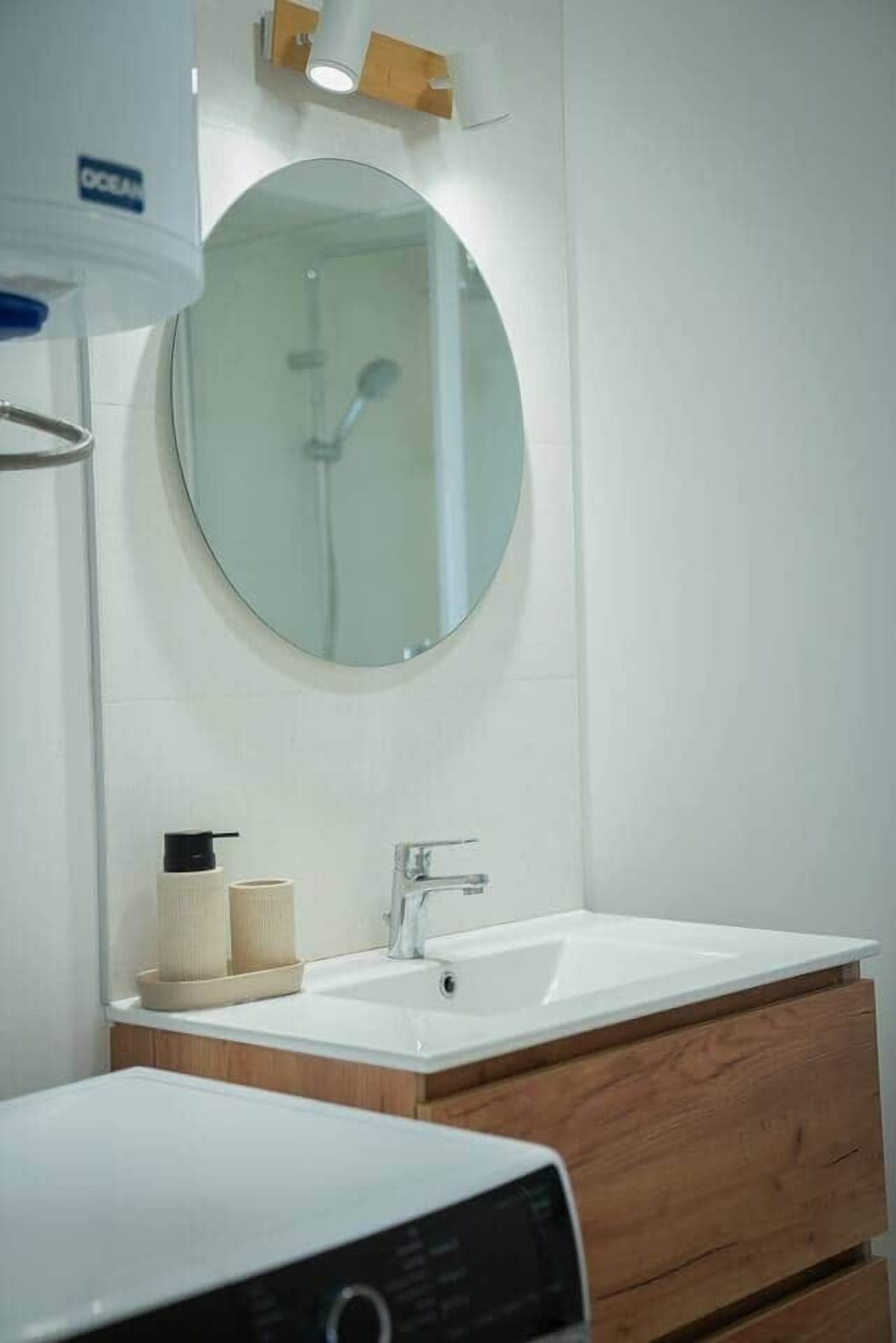 Un baño con un espejo redondo, dos lavamanos, un tocador de madera y un inodoro.