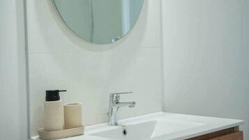 Un baño con un espejo redondo, dos lavamanos, un tocador de madera y un inodoro.
