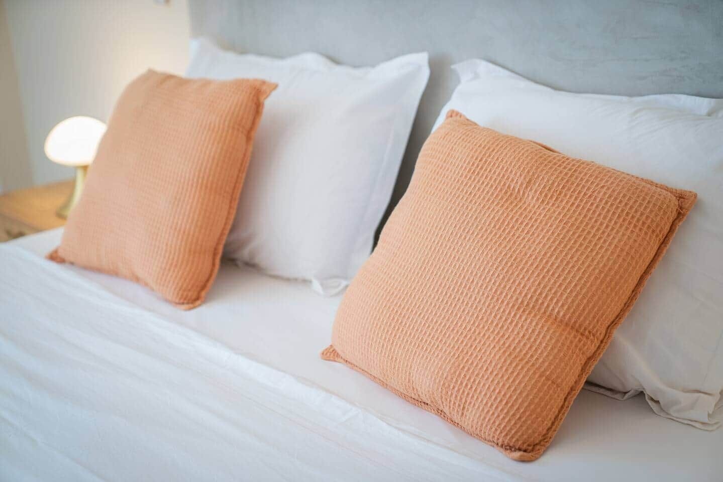 Een bed met witte beddengoed en twee oranje kussens.