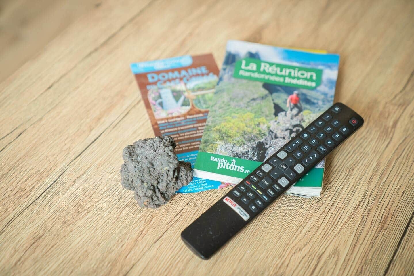 Une télécommande, un livre intitulé « La Réunion », et une brochure sur une surface en bois.