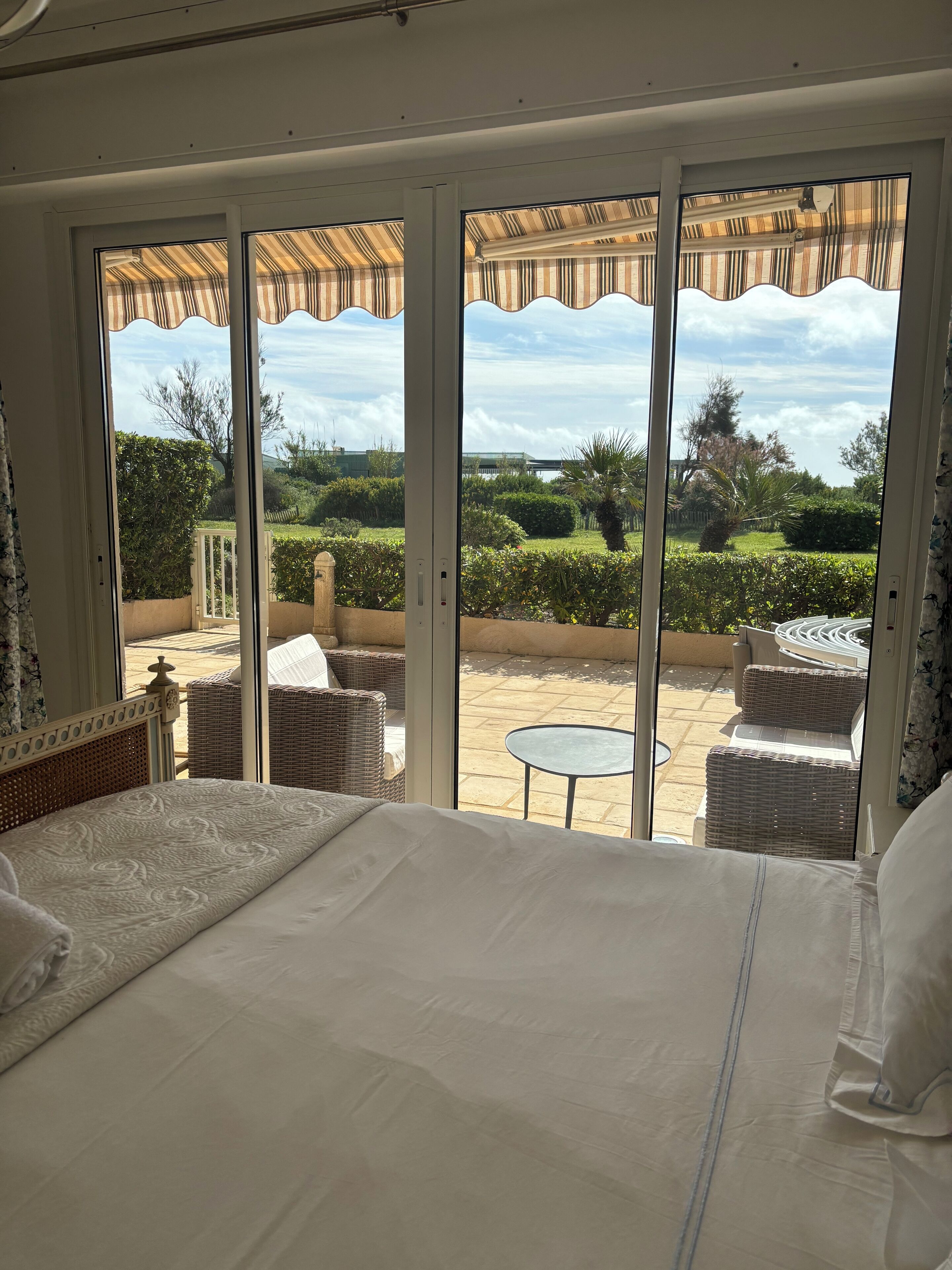 A bedroom with a large bed, a view of a patio with wicker furniture, and a glass door leading to an outdoor area.