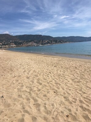 Ein Sandstrand mit ruhiger See und einer Stadt im Hintergrund.