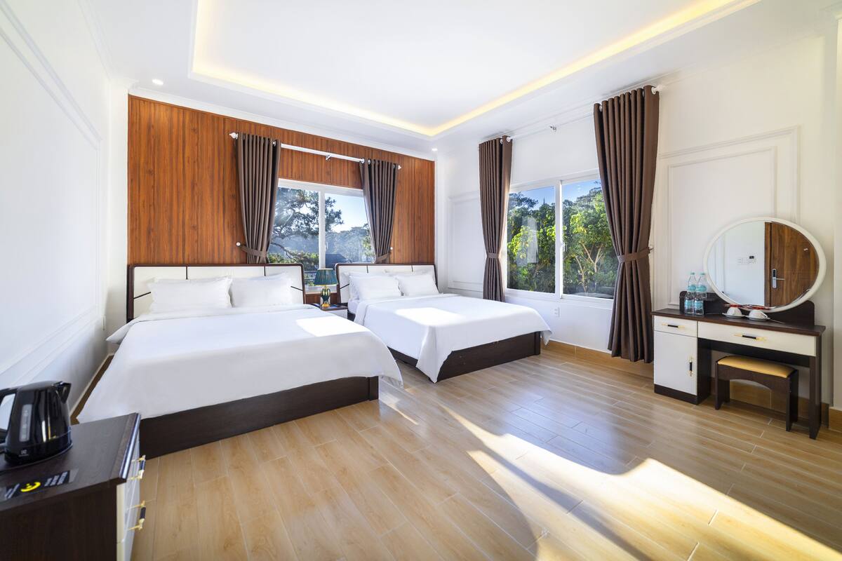 A hotel room with two beds, a desk, a chair, a mirror, and a window with curtains.