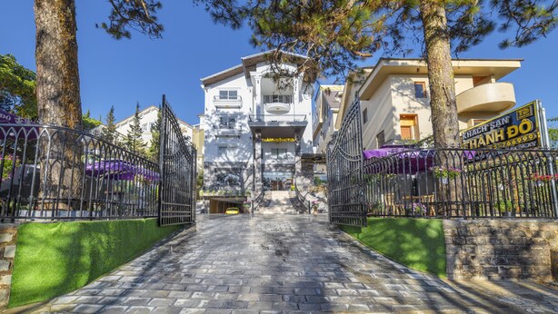 A hotel entrance with a stone pathway leading to a white building with balconies. - Thanh Do 1 Hotel (Xuan Huong - Da Lat)