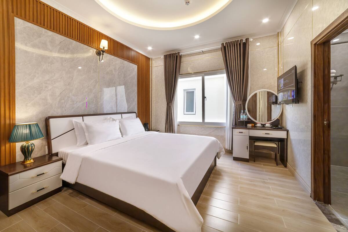 A hotel room with a large bed, a vanity with a mirror, a television, and a window with curtains.