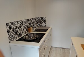 Una cucina con piano cottura a gas, un lavandino e un vassoio con quattro bicchieri di metallo. Sul bancone ci sono due barattoli e lo schienale è decorato con un motivo bianco e nero.