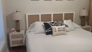 Ein ordentlich bezogenes Bett mit einer weißen Tagesdecke und zwei Kissen, eines mit einem Meeresmotiv. Vier an der Wand befestigte Kunstwerke zeigen Bäume.