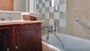 Un baño con tocador de madera, cabina de ducha con mampara de vidrio y bañera.