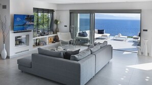 Un soggiorno moderno con un divano grigio, una TV a schermo piatto e un'ampia finestra con vista sul mare.