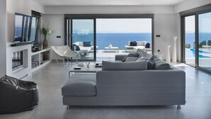 Un soggiorno moderno con un divano grigio, una TV a schermo piatto e una grande finestra con vista sul mare.