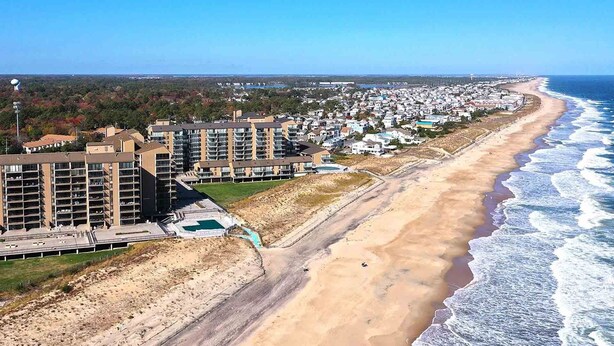 Een woongebied aan de kust met meerhoogbouwwoningen, een zandstrand en een helder uitzicht op de oceaan.