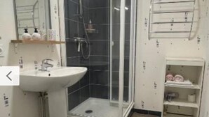 Et badeværelse med en hvid vask, en brusekabine med glasvægge og en lille hylde med toiletartikler.