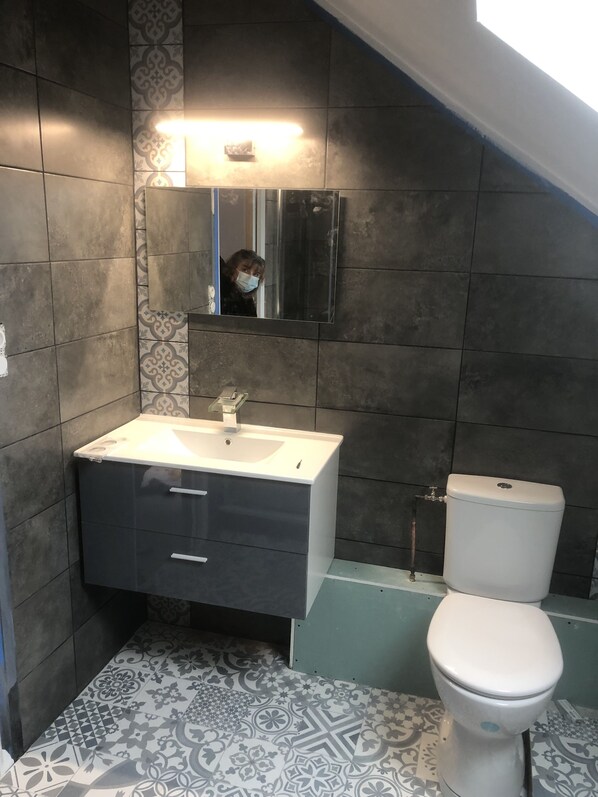A bathroom with a white sink, dark cabinets, a toilet, and patterned floor tiles.