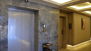 A modern elevator with a marble wall, a digital display, and a small trash bin.