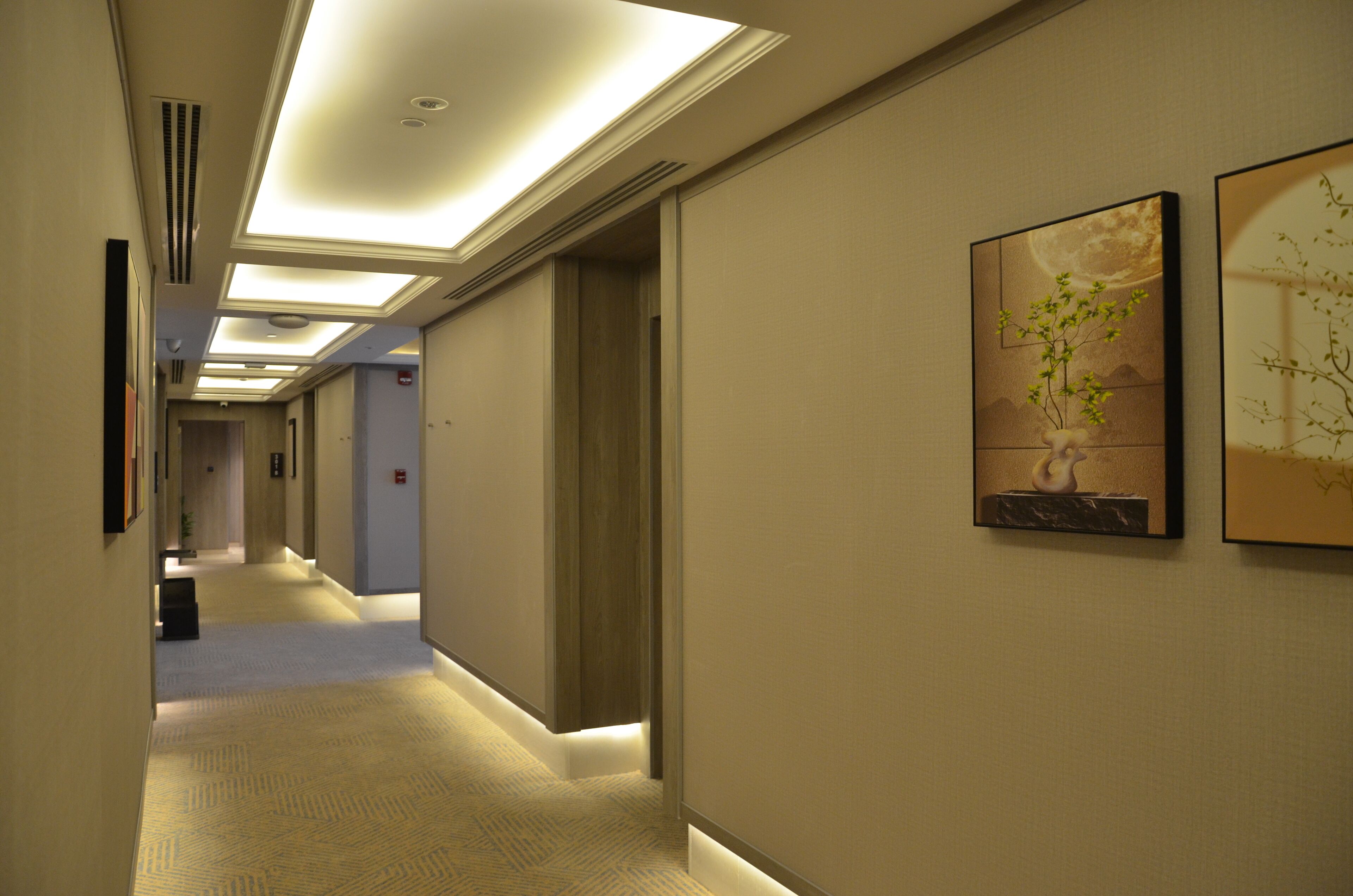 A hotel hallway with a carpeted floor, recessed lighting, and framed artwork on the walls.