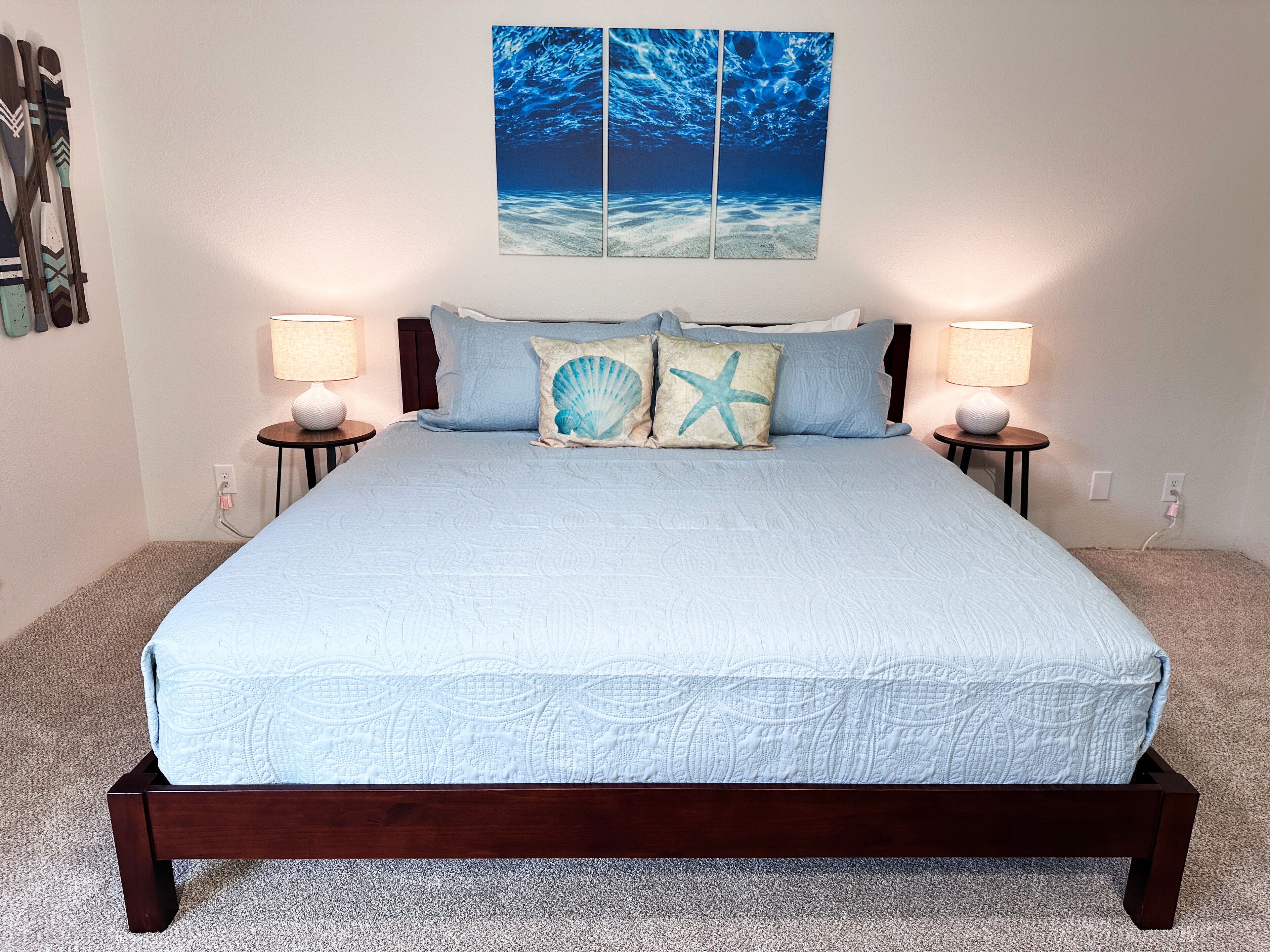 Un lit recouvert d’une couette bleu clair, deux tables de chevet avec des lampes et une décoration murale représentant une scène sous-marine.