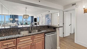 A modern kitchen with granite countertops, stainless steel appliances, and wooden cabinets. - Beach Vibes, Beachfront Penthouse, Pelican Beach Resort (Destin)