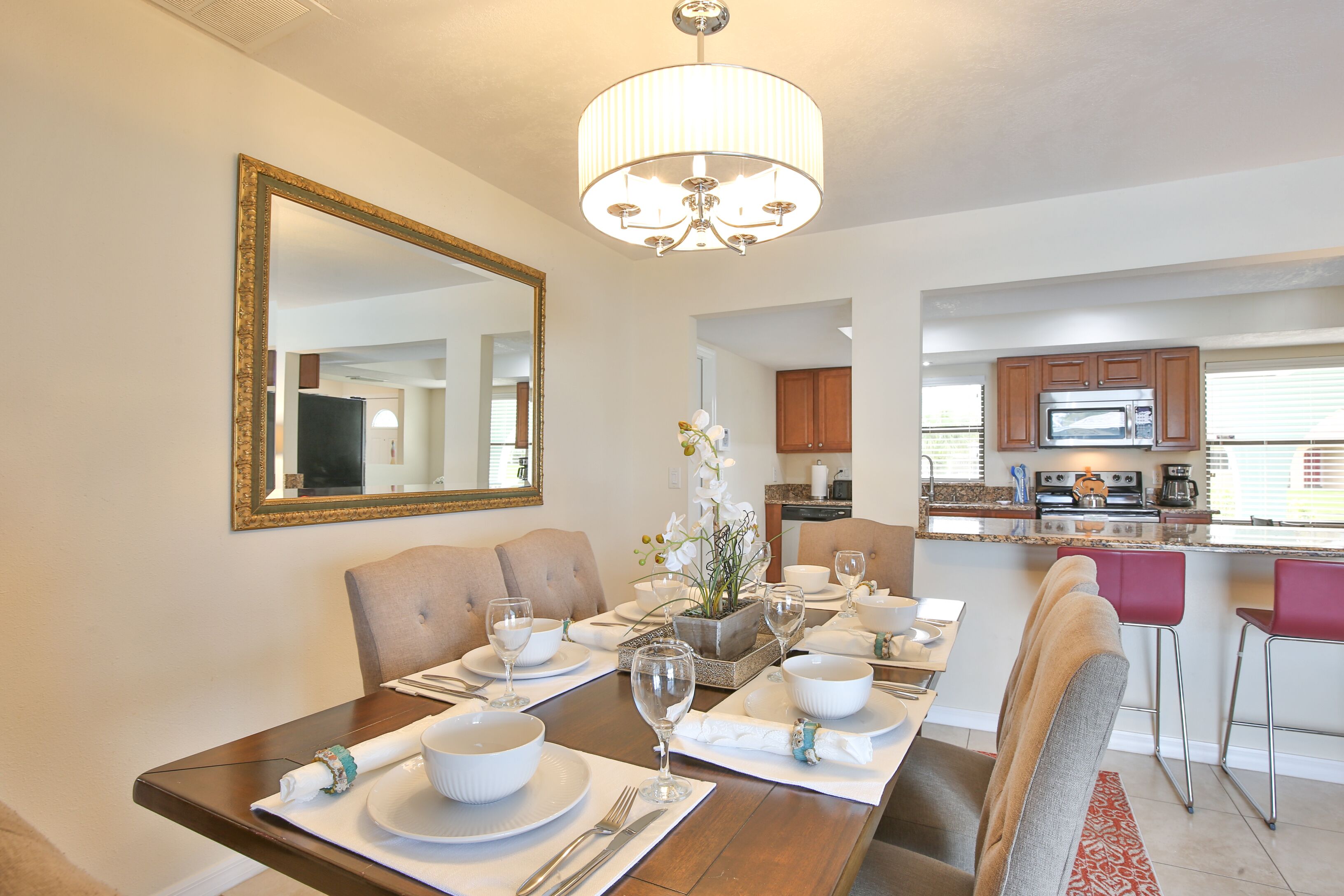 Un coin repas avec une table en bois dressée pour quatre personnes, un lustre et une cuisine en arrière-plan.