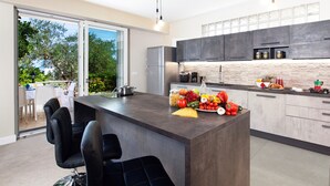 Une cuisine moderne dotée d’un grand îlot central, de meubles de couleur sombre et offrant une vue sur l’extérieur.