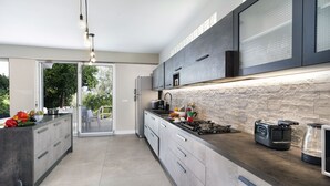 Une cuisine moderne dotée d’un pare-feu en pierre, d’appareils électroménagers en acier inoxydable et d’un grand îlot central avec un four encastré.