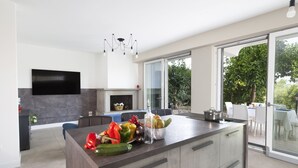 Une cuisine moderne dotée d’un grand îlot central, d’un téléviseur à écran plat et d’une porte vitrée donnant sur un espace extérieur.