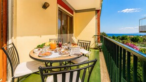 A balcony with a table set for breakfast, chairs, a window, and a view of the sea. - AMORE RENTALS - Appartamento Sally with Terrace and Partial Sea View (Sorrento)