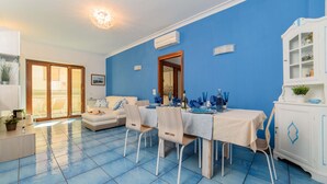 A dining area with a table set for four, a white cabinet with glass doors, and a blue-tiled floor. - AMORE RENTALS - Appartamento Sally with Terrace and Partial Sea View (Sorrento)