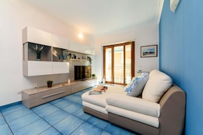 A modern living room with a sofa, a TV, and a dining area with a table and chairs. - AMORE RENTALS - Appartamento Sally with Terrace and Partial Sea View (Sorrento)