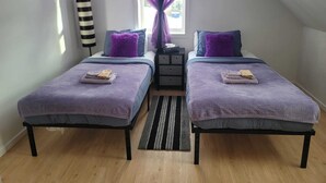 Une chambre avec deux lits, une fenêtre ornée de rideaux violets, une lampe noire et un tapis à rayures.