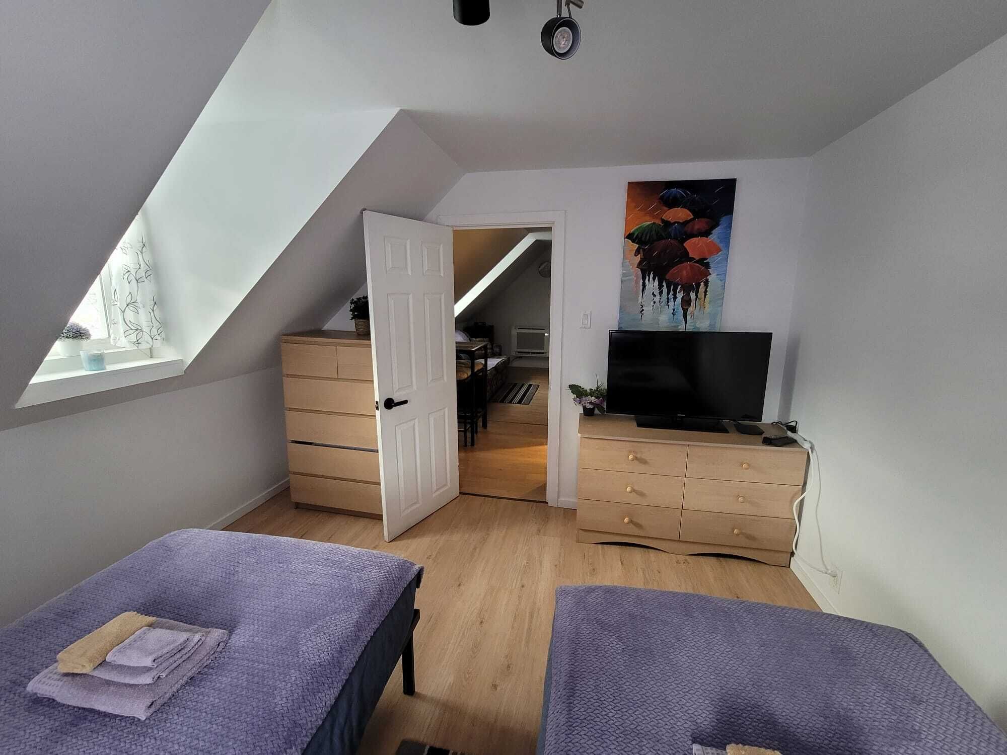 Une chambre avec un plafond en pente, une télévision, une commode et un tableau.