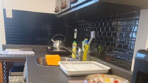 Une cuisine avec un plan de travail noir, une bouilloire, un égouttoir et un saladier rempli de fruits.