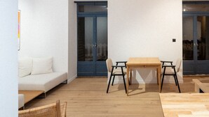 Un intérieur moderne avec une table à manger en bois, deux chaises, un banc en osier, un canapé blanc et une porte bleue.