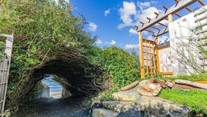 A rustic wooden archway leading to a beach, surrounded by greenery and a wooden pergola.