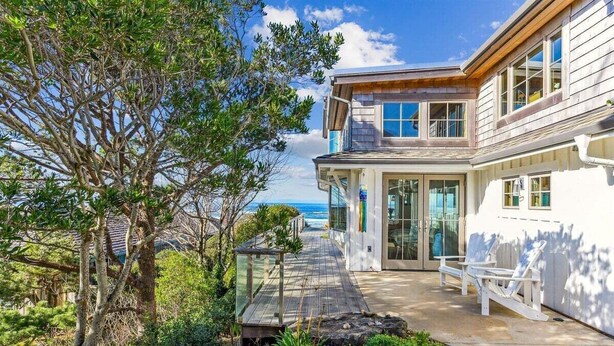 A coastal house with a deck, a view of the ocean, and a patio area with chairs.